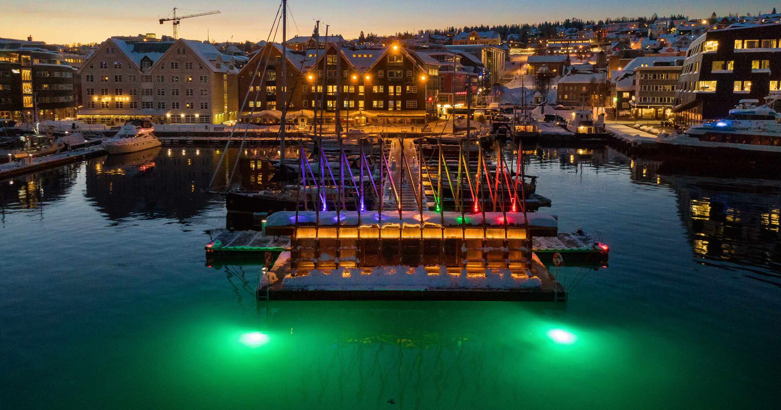 PUST’s floating sauna illuminated in Tromsø harbour at dusk.